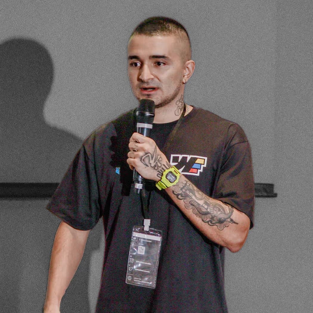 Styven on stage at a conference, holding a microphone and wearing an event lanyard.